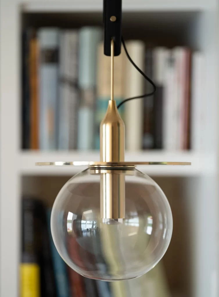 Brass, Glass globe and black leather light fixture detail in front of bookshelf.