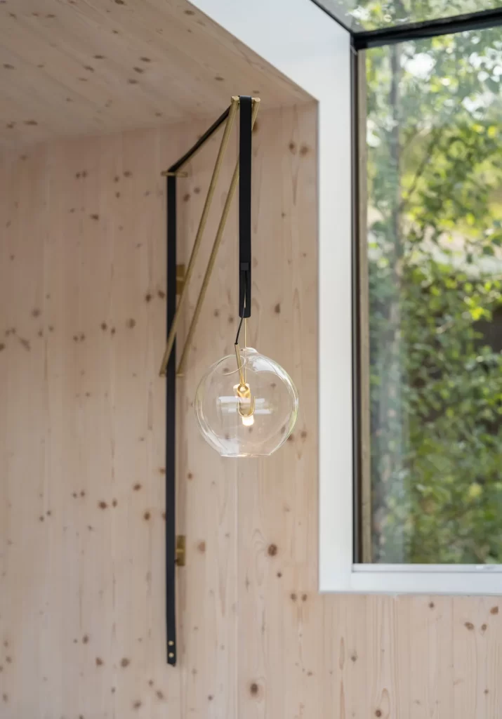 Viabizunno light fixture including brass, black leather and glass globe in front of cross laminated timber wood wall.