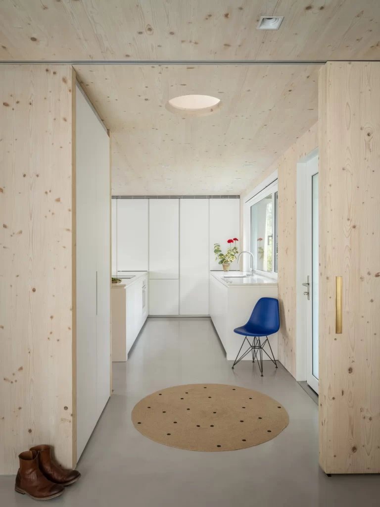 Bright blue chair sits in a white modern kitchen surrounded by warm cross laminated timber (CLT) wood walls and ceilings.