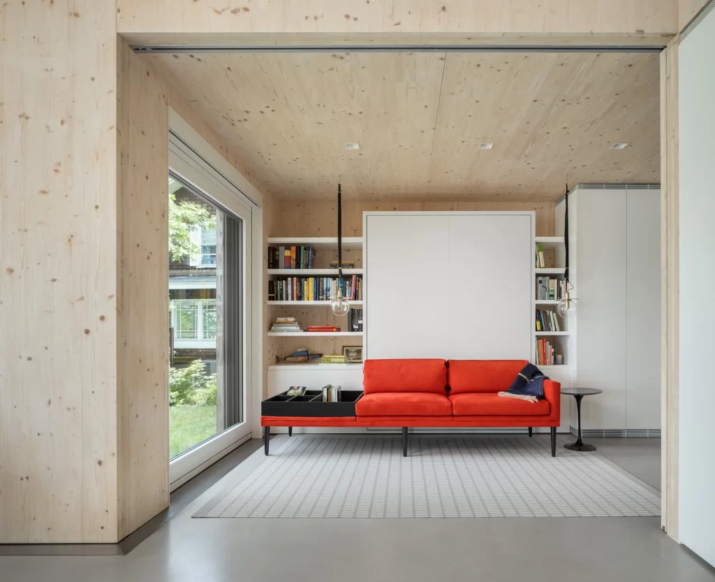 Cross Laminated Timber Interior walls and ceilings and large triple paned glass door frame a bright red couch in this modern living space..