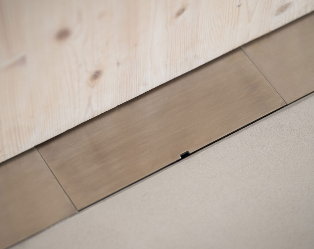 Image of closed metal electrical chase inset into floor to house outlet.