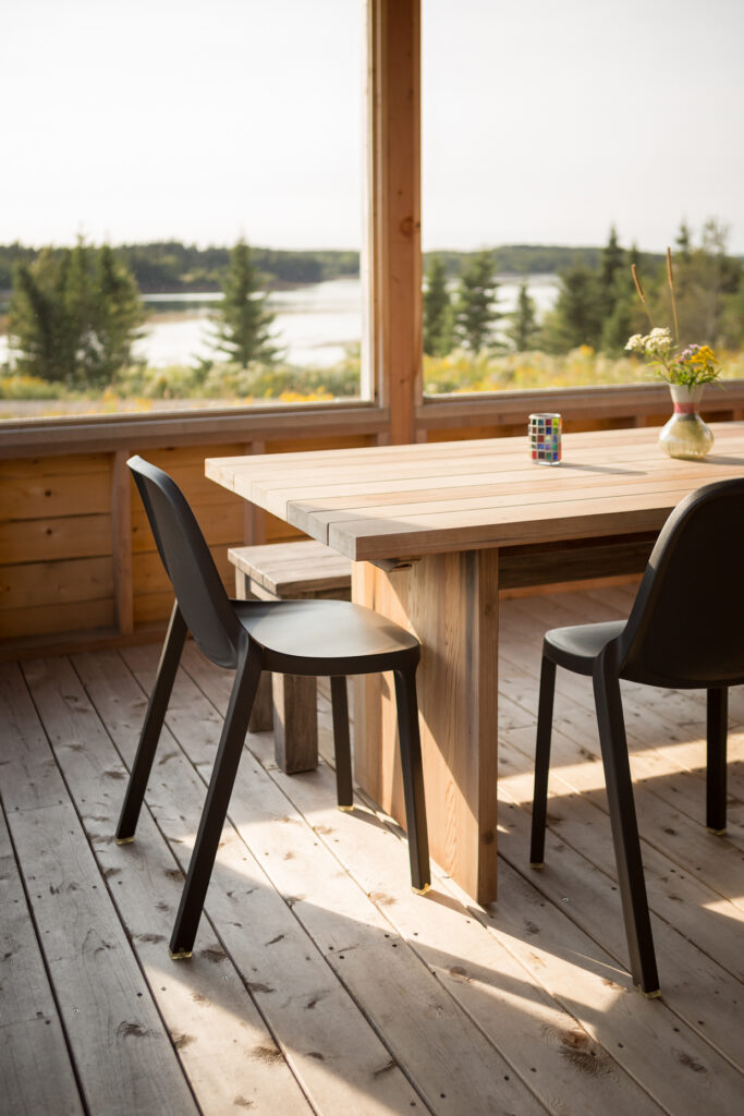 Coastal Maine view of ocean and evergreens, seen from a wood screened in porch with wooden table.
